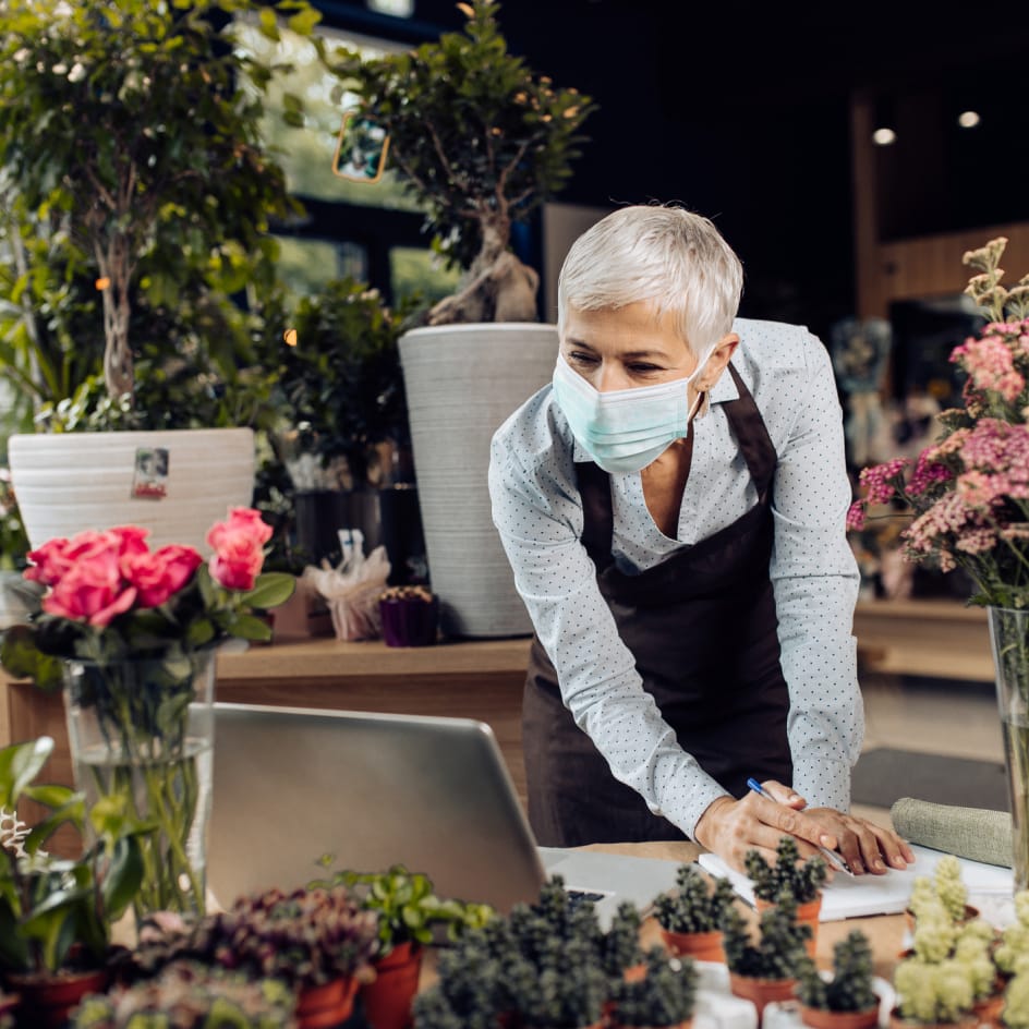 Woman in mask surrounded by flowers taking notes.